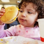 Kid eating fast food burger - A new study shows that foods high in fat and sugar can dumb down young kids later in life.