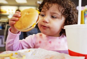 Kid eating fast food burger - A new study shows that foods high in fat and sugar can dumb down young kids later in life.
