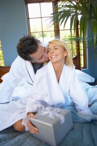 Couple on bed, man giving woman a wrapped gift.