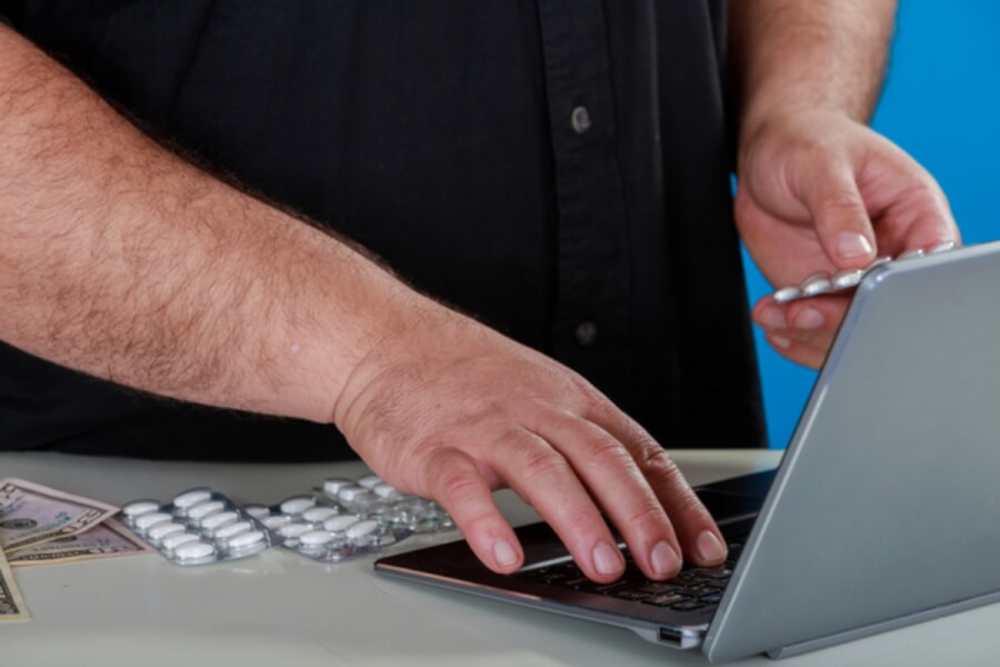 Person typing on a laptop holding pill packets.