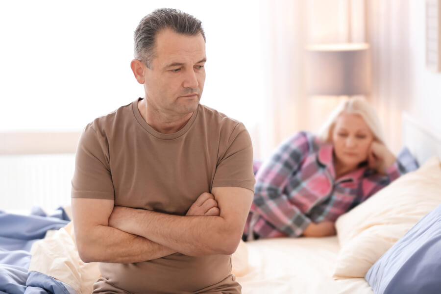 Man sitting at the edge of his bed appearing frustrated.