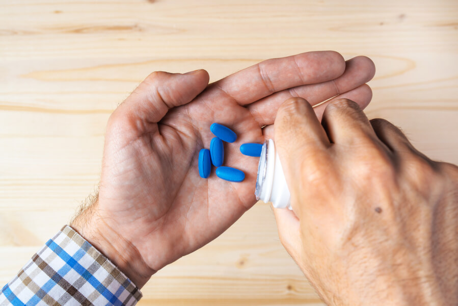 Person pouring blue pills into his hand from a plastic container.