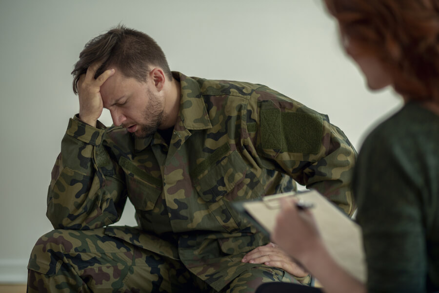 Man in military fatigues sitting with his hand on his head.