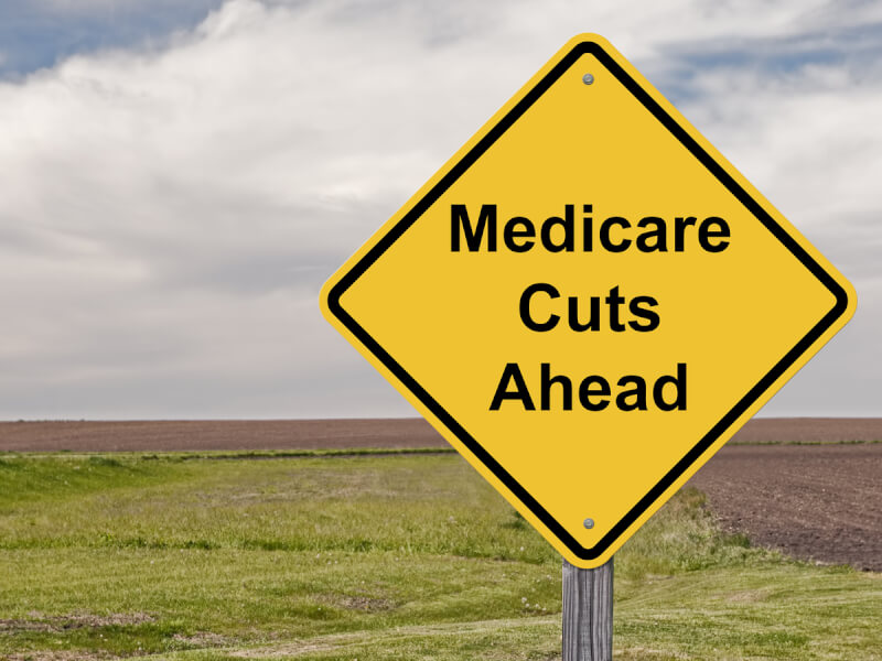 Yellow diamond road side labeled Medicare cuts ahead.