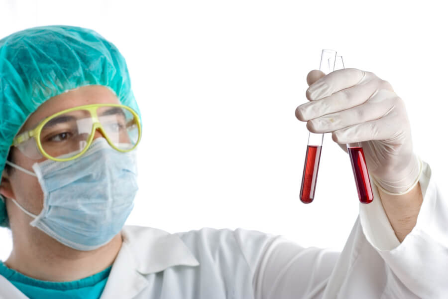 Technician wearing a facial mask and holding glass tubes with liquid.