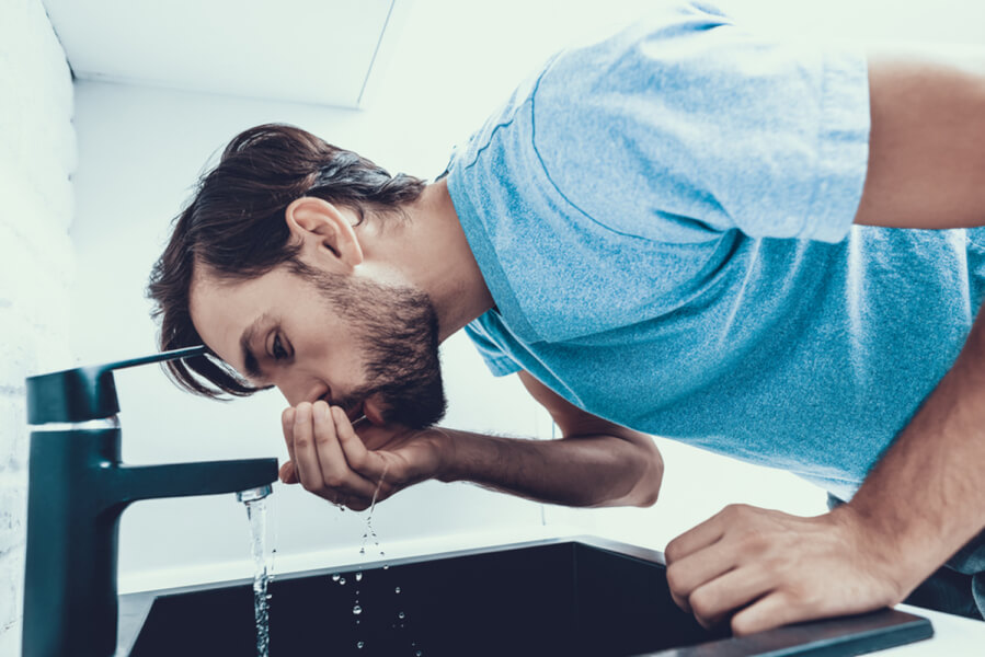 Man drinking water over a sink from his palm.