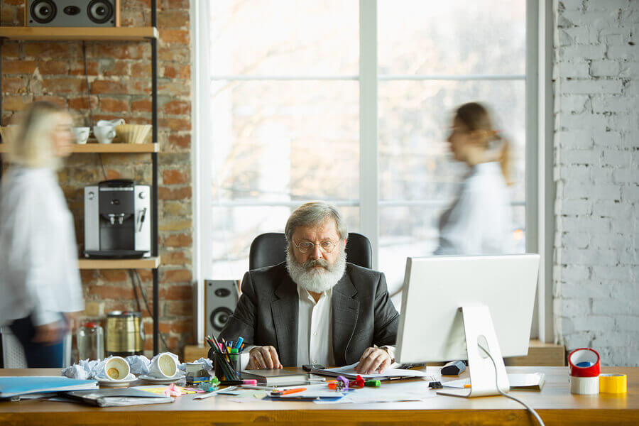 Man sitting at a desk filled with papers and a desktop computer.