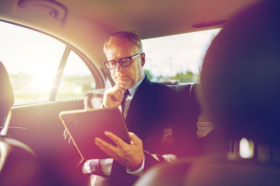 Man in the back seat of a car looking at his tablet.
