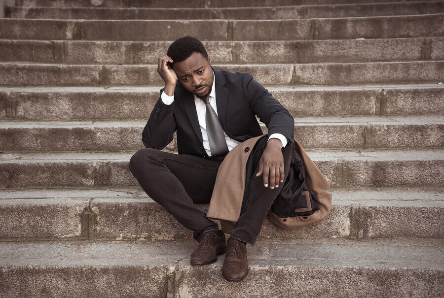 Man sitting on steps with his hand on his forehead.
