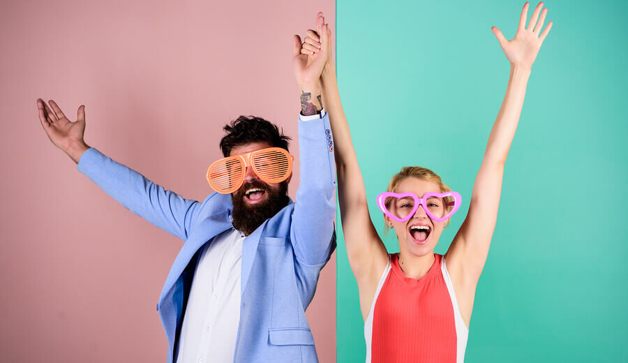 Couple wearing funny glasses holding their hands up.