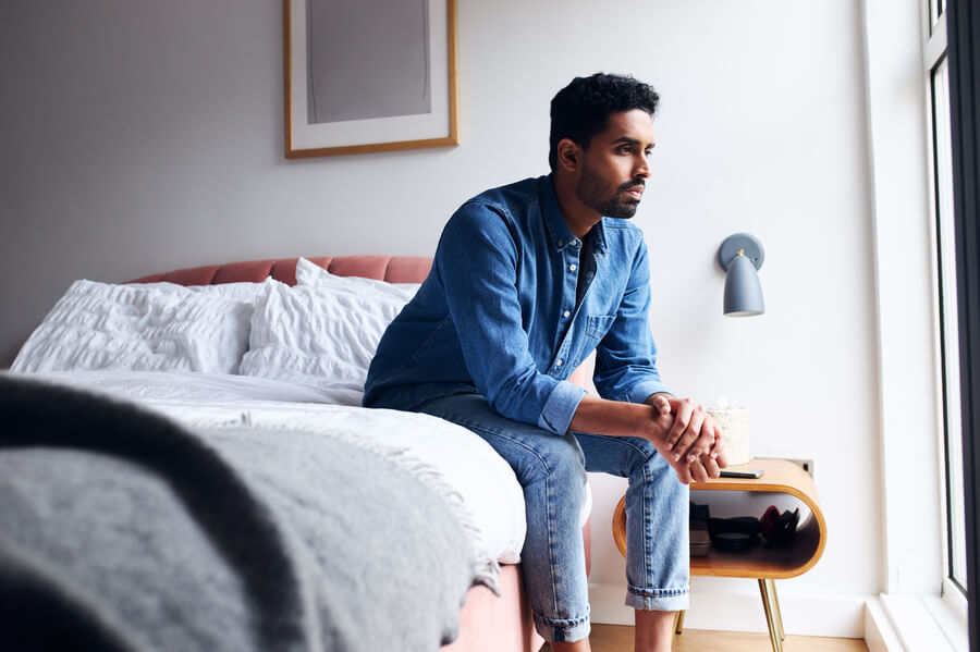 Man sitting at the edge of his bed looking out the window