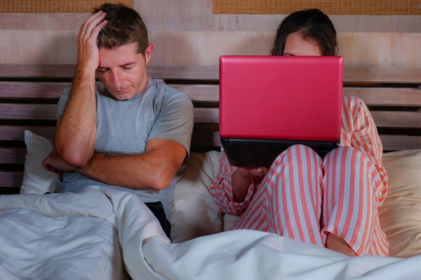 Woman on her laptop next to her partner in bed Woman on her laptop next to her partner in bed