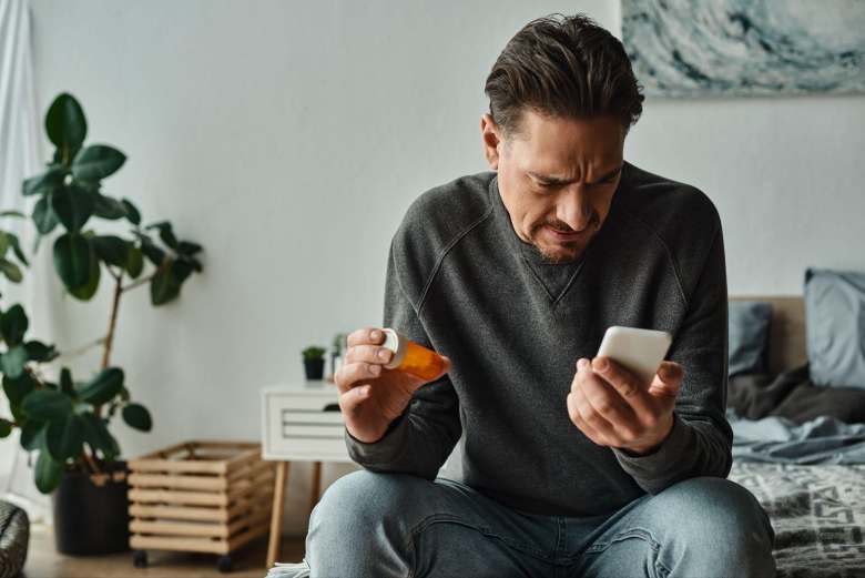 man holding a bottle of pills and researching on his phone the risks and side effects