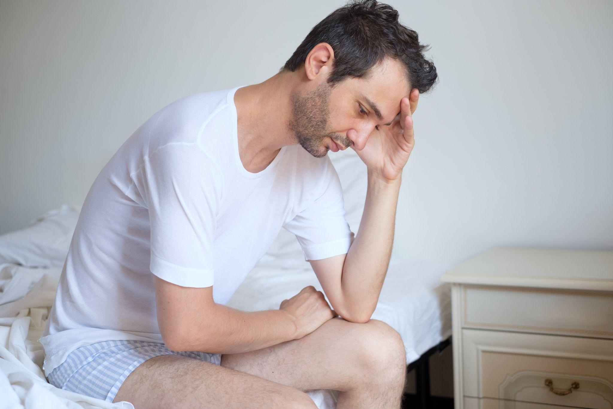 a worried man sitting at the edge of a bed
