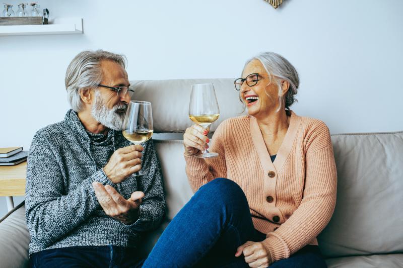 elderly couple laughing and drinking wine at home
