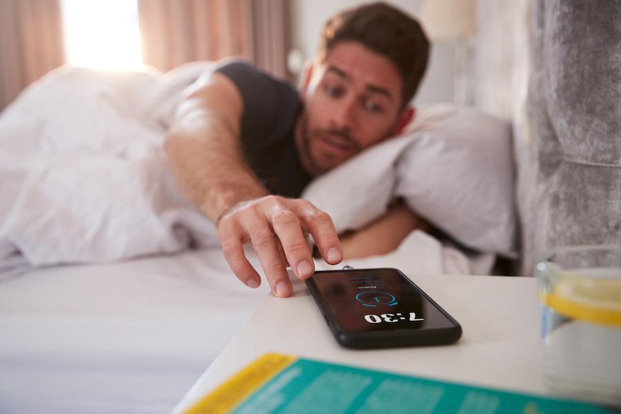 man in bed reaching for his phone
