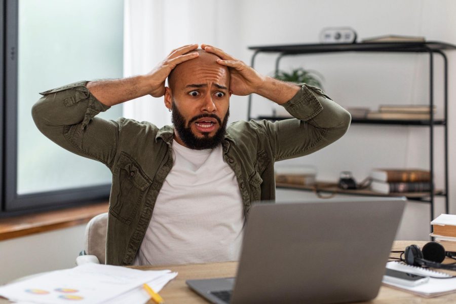 bald man sitting at a desk with a surprised look staring at a laptop