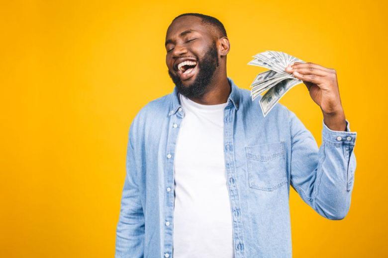 young smiling man using dollar bills to fan himself
