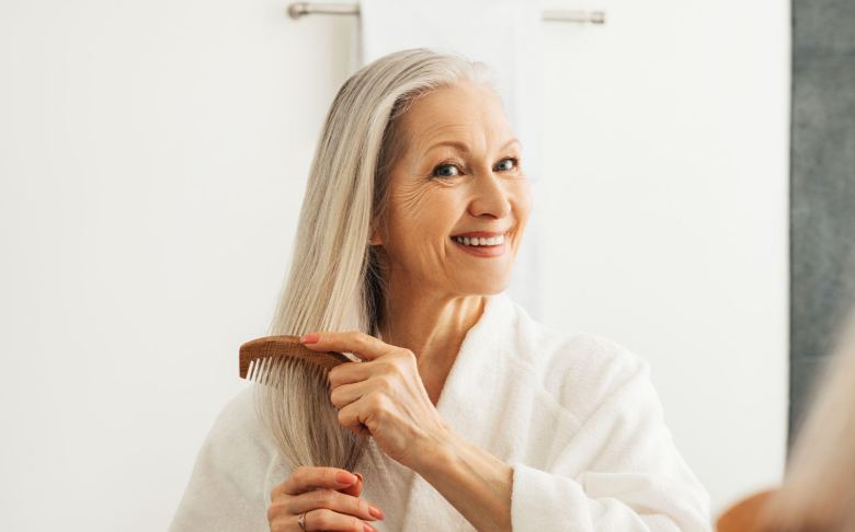 middle-aged woman combing her long white hair with a big smile