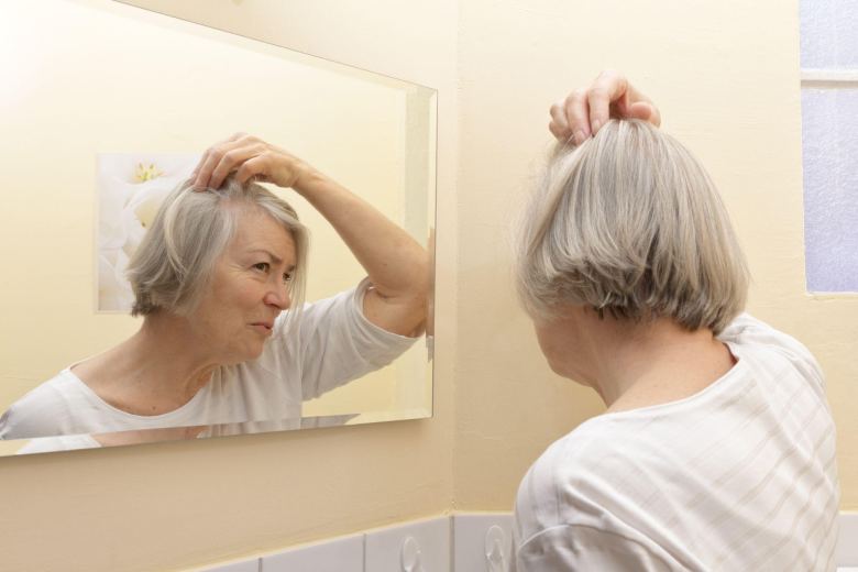 senior lady checking her scalp in a bathroom mirror