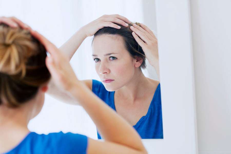 young girl checking her hairline in a bathroom mirror for hair loss signs