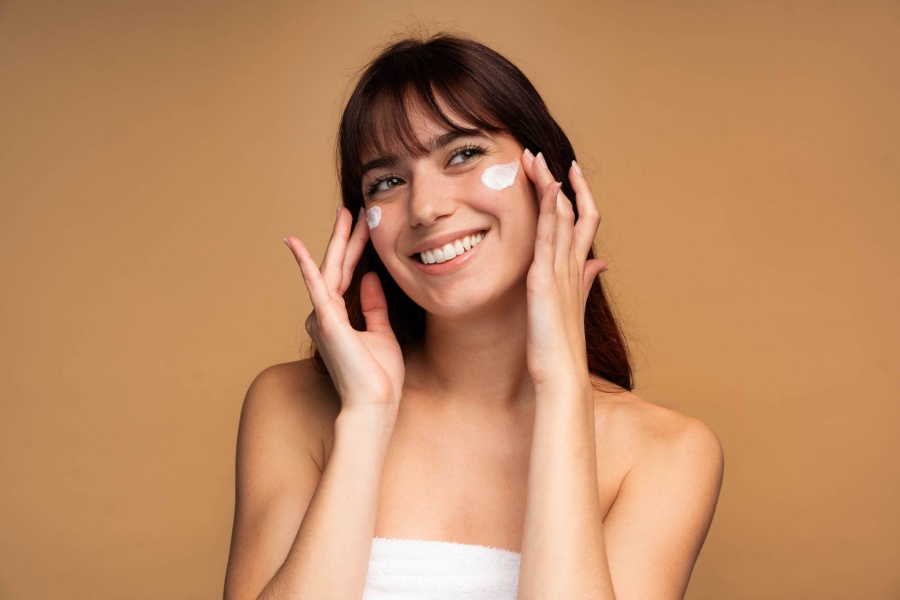 Smiling woman applying skincare cream to cheeks