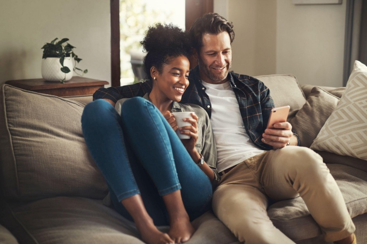 Cheerful couple relaxing on a couch, looking at a smartphone together