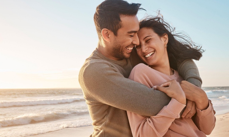 Joyful couple embracing on a windy beach at sunset