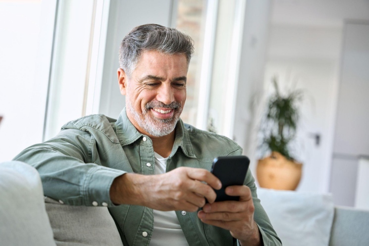 Smiling middle-aged man using a smartphone while sitting on a couch