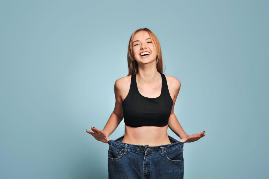 Happy woman showing weight loss results by holding out oversized jeans