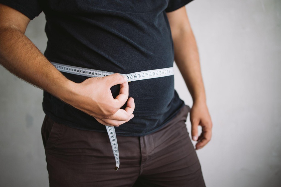 Man measuring waist circumference with a tape measure for weight loss tracking