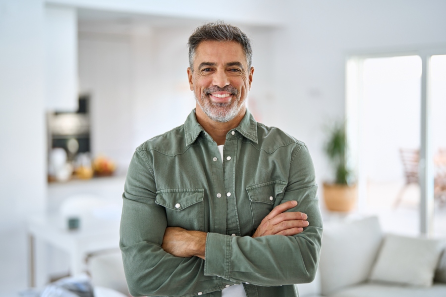 Confident middle-aged man smiling with arms crossed at home