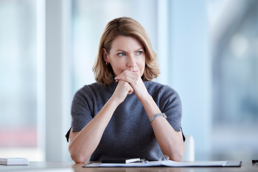 Thoughtful businesswoman resting chin on hands at office desk.