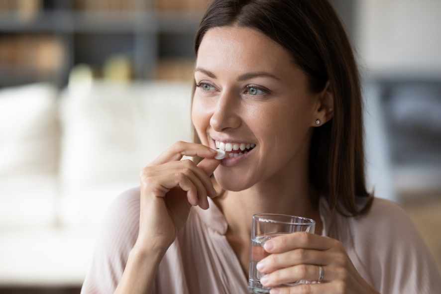 Close up smiling woman taking pill, holding water glass