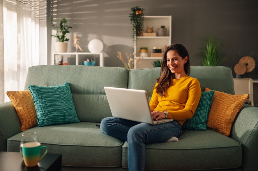 Smiling woman sitting on couch with laptop.